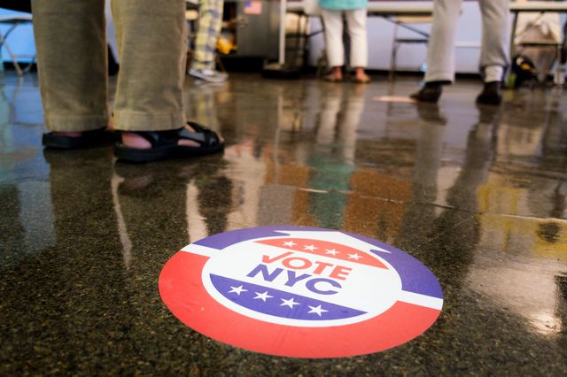 A photograph of a sign that says "NYC Votes" on the floor of the polling site